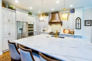 Remodeled kitchen with large island, white cabinets and white stone countertops. Pendent lighting over island. Wood floors.