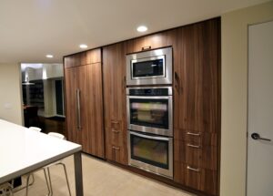 Remodeled modern kitchen with woodgrain cabinets and stacked ovens.