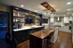 Remodeled kitchen with wood floors, black modern cabinets, long island in middle with butcher-block countertop.